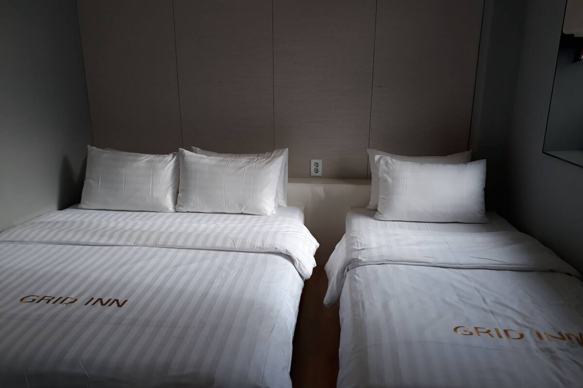 A hotel room with two beds, each with a white bedspread and pillows, and the room has a neutral color scheme.