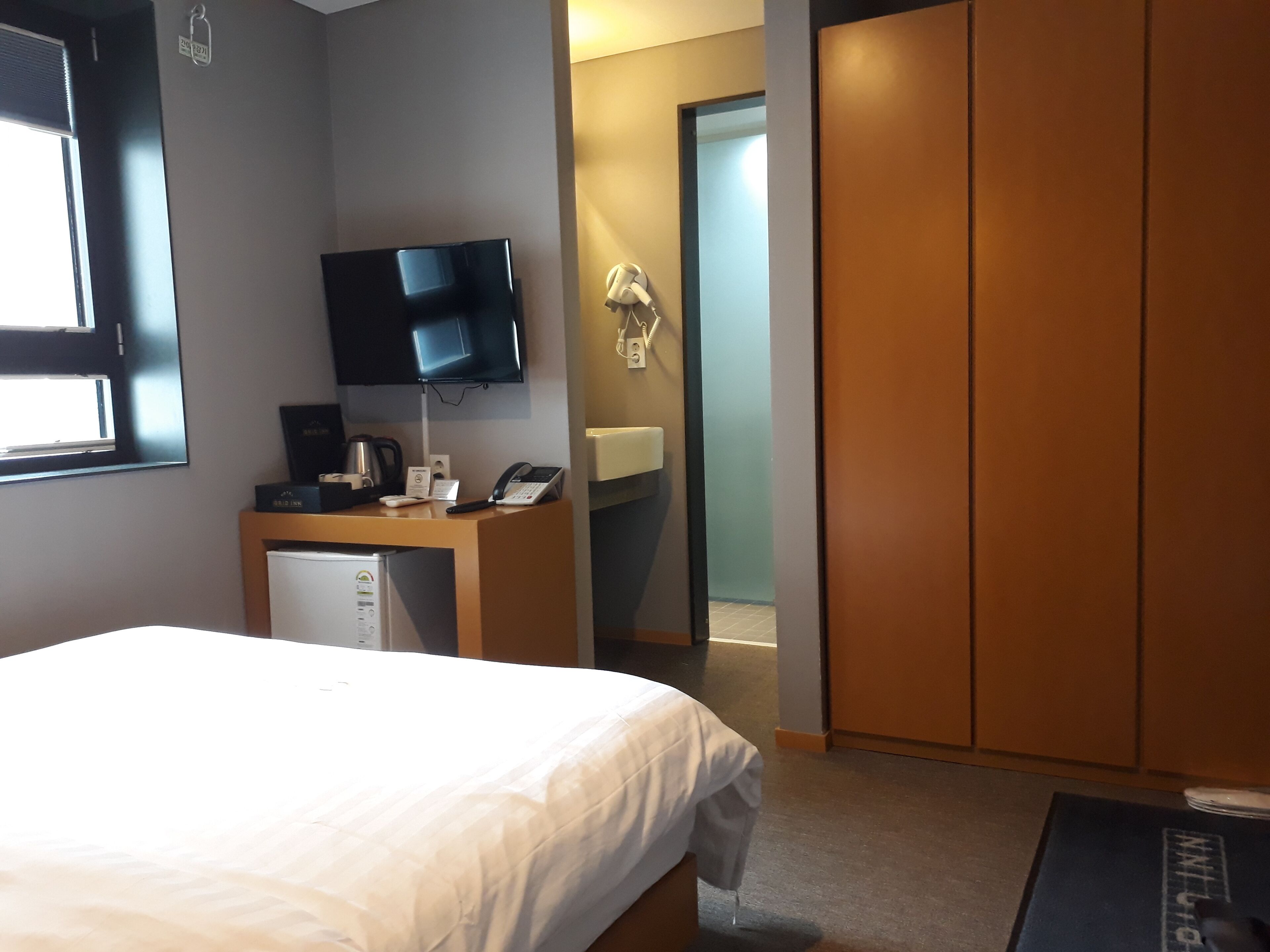 Une chambre d’hôtel comprenant un lit, un bureau avec un téléphone et une machine à café, un téléviseur fixé au mur et une armoire.