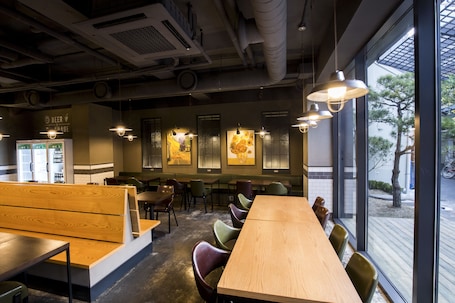 A restaurant with wooden tables and benches, large windows, and hanging pendant lights.