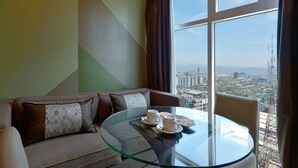 Ett modernt hotellrum med ett glasbord, en soffa och utsikt över stadsbilden.