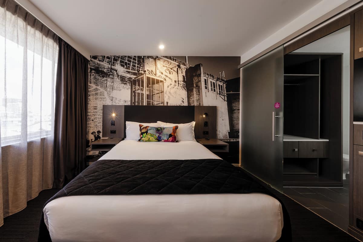 Una moderna camera d'albergo con un letto grande, un comodino, un armadio e un'ampia finestra con tende.