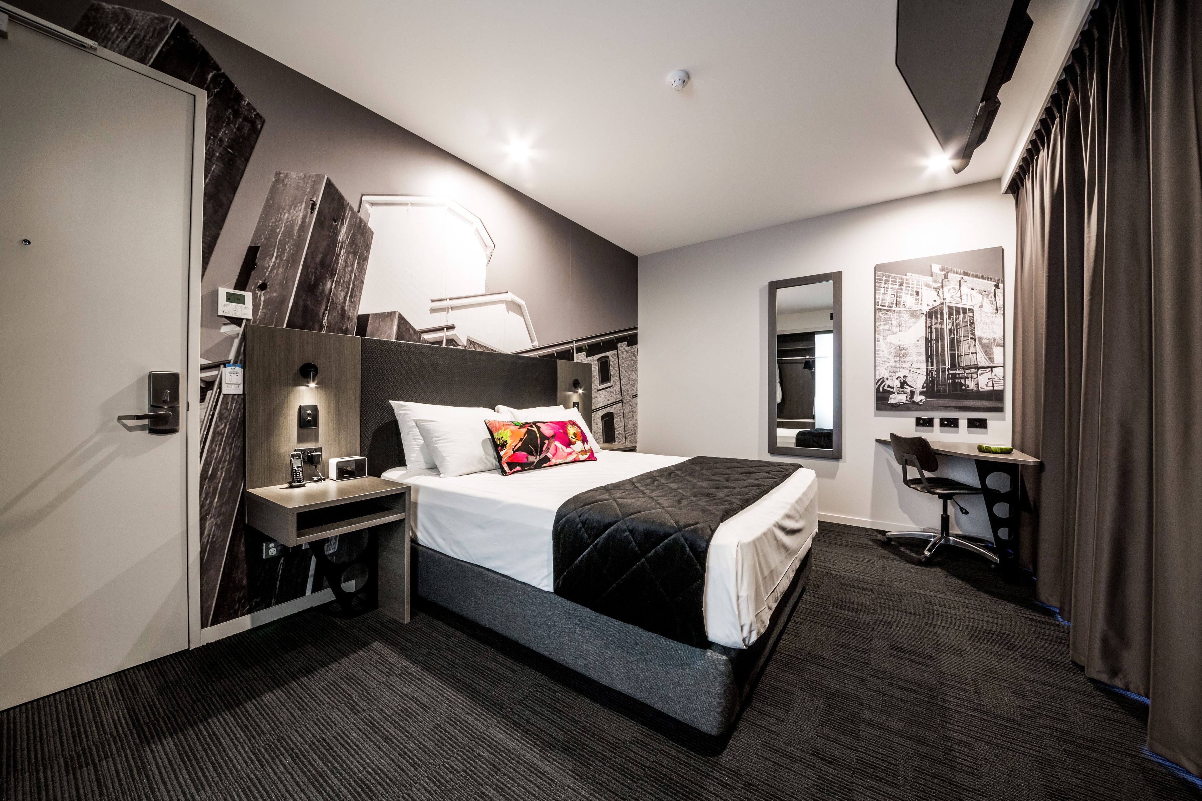 A modern hotel room with a large bed, bedside tables, a desk, and a chair.