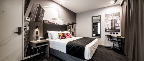 A modern hotel room with a large bed, bedside tables, a desk, and a chair.