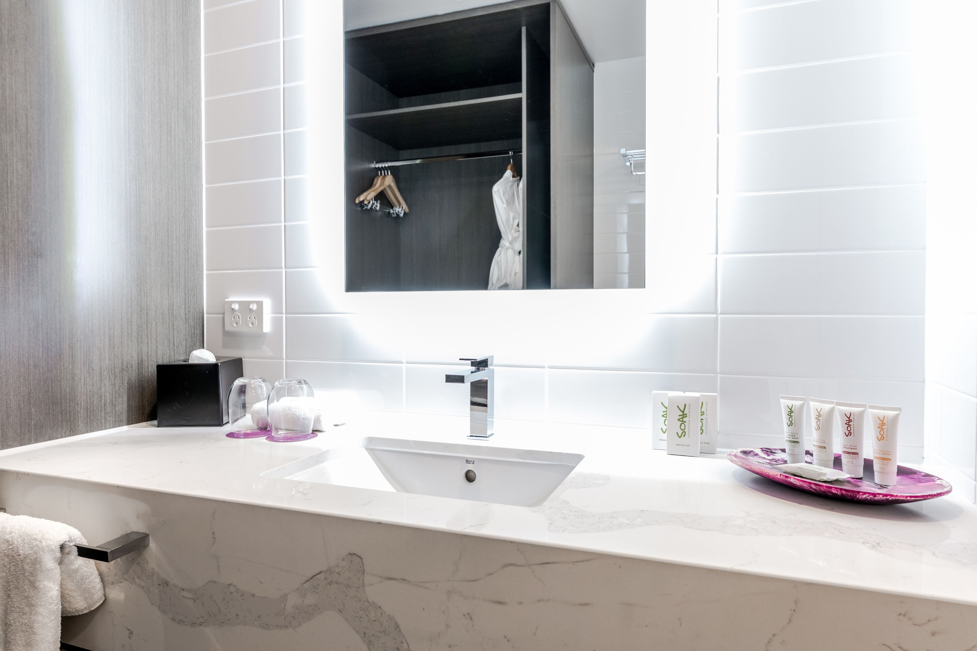 Un baño moderno con un lavabo blanco, un espejo grande y una zona de tocador con artículos de aseo.