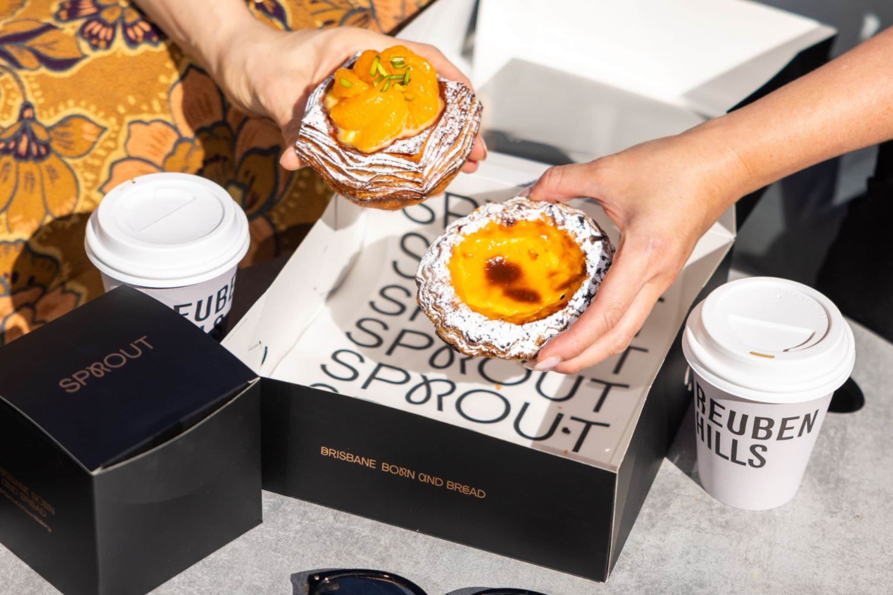 A person holding two pastries, a box labeled "SPROUT," and a coffee cup with "BEUBEN HILLS" text.