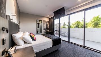 A modern hotel room with a large bed, a desk, a telephone, and a view of the outdoors through large windows.