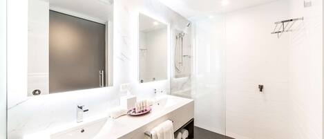 Un baño moderno con tocador de mármol blanco, un espejo grande y cabina de ducha con paredes de vidrio.