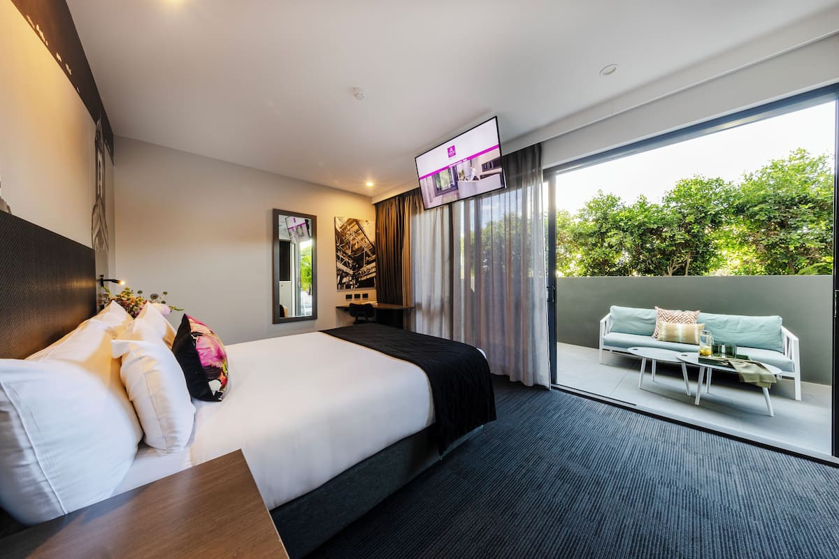 Una camera d'albergo moderna con un letto grande, una scrivania, una televisione a schermo piatto e un balcone con divano.