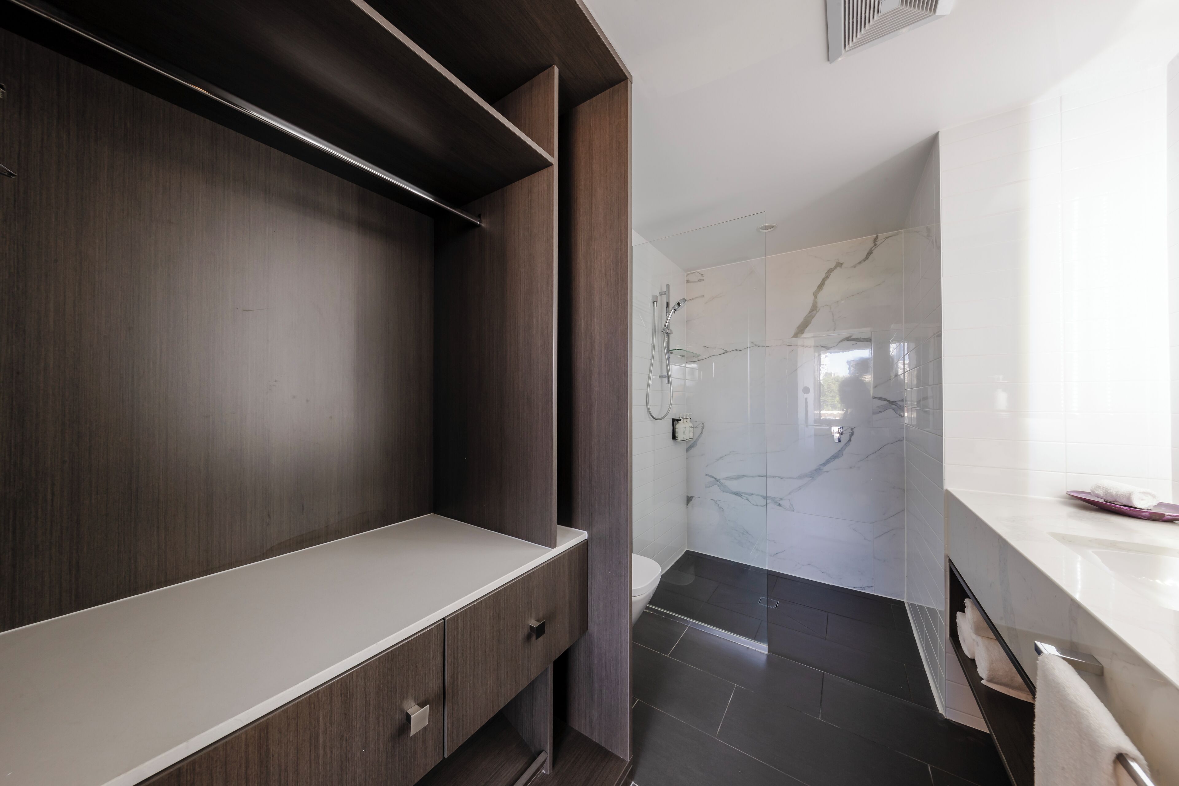 A modern bathroom with a dark wood vanity, a white countertop, and a glass shower enclosure with marble tiles.