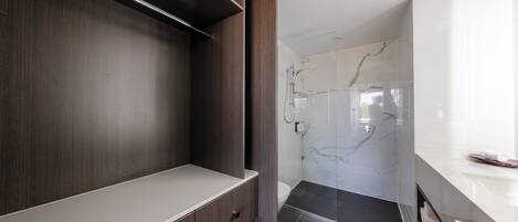 A modern bathroom with a dark wood vanity, a white countertop, and a glass shower enclosure with marble tiles.