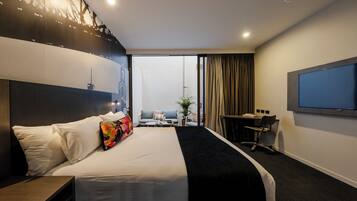 A hotel room with a large bed, a desk, a chair, a TV, and a view of the city.