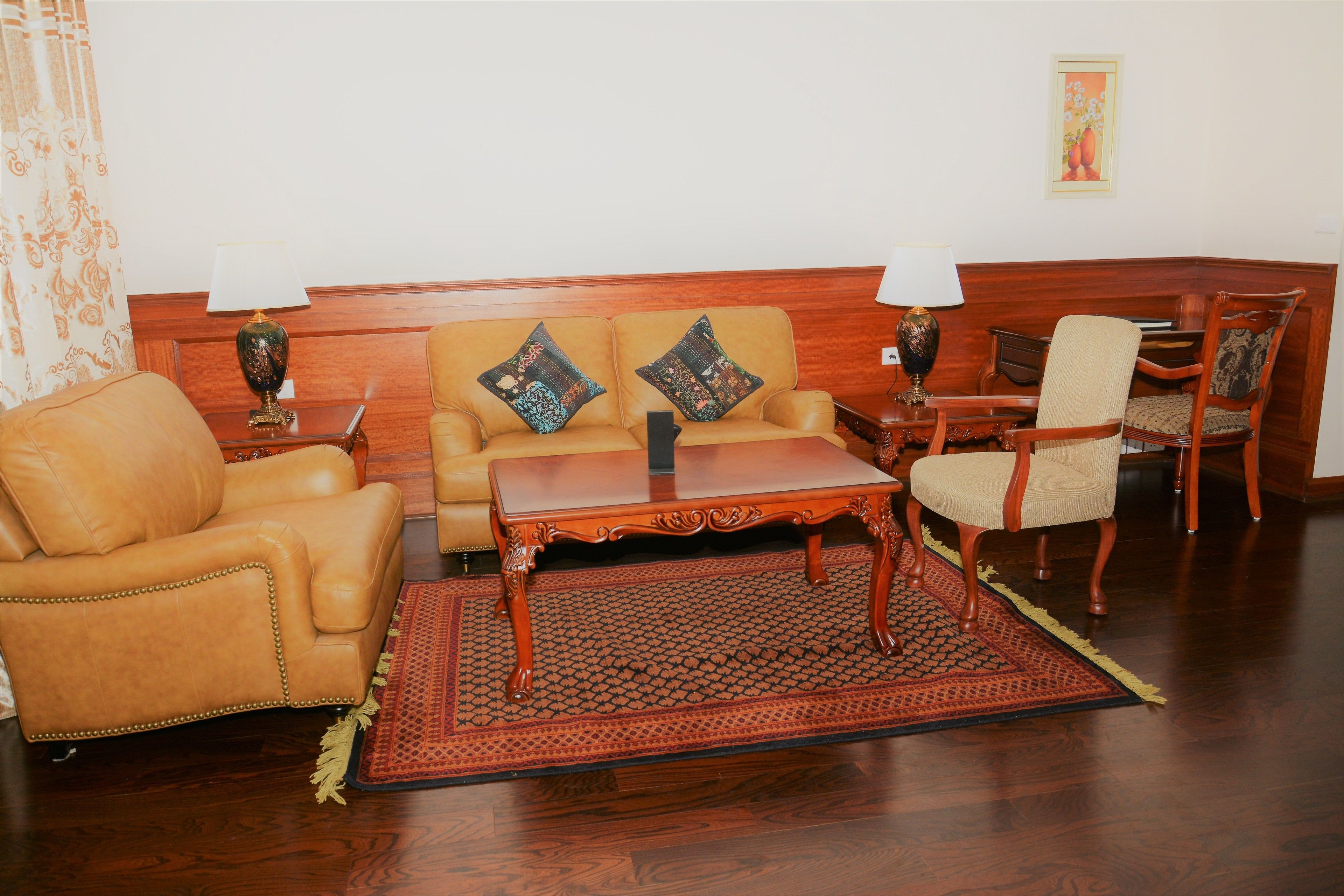 Un salón con sofá, sillón y una mesita de centro, suelo de madera y alfombra estampada.