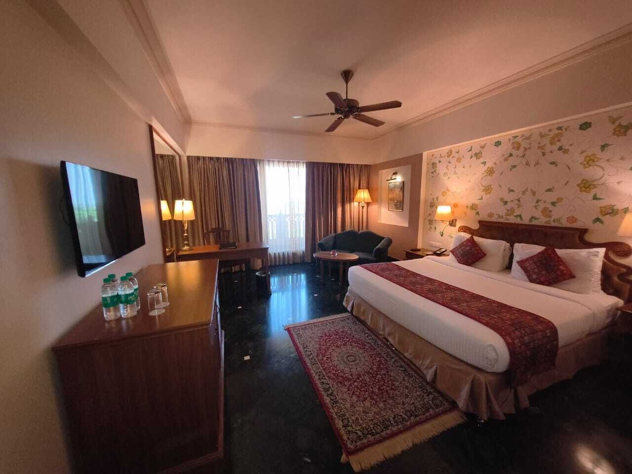 Una habitación de hotel con cama, escritorio, silla, televisor y ventilador de techo.