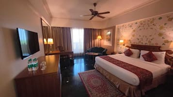Ein Hotelzimmer mit Bett, Schreibtisch, Stuhl, Fernseher und Deckenventilator.