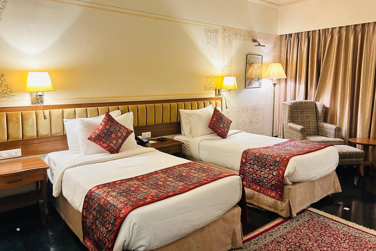 A hotel room with two beds, each with a red patterned bedspread, a wooden headboard, and a nightstand with a lamp.