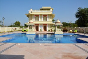 A large swimming pool with a geometric design, surrounded by a building with multiple balconies and a traditional architectural style. - Indana Palace Jaipur (Amer)
