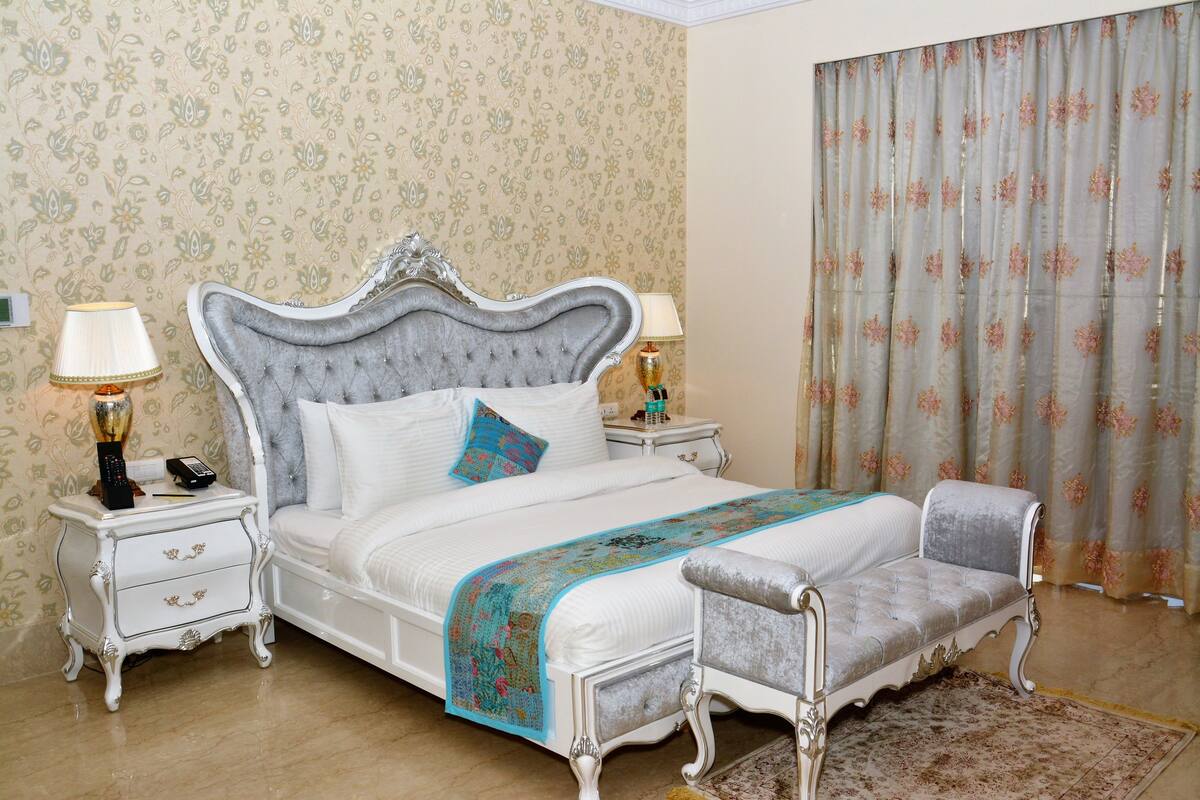 A bedroom with a large bed, two bedside tables, a chair, and a window with curtains.
