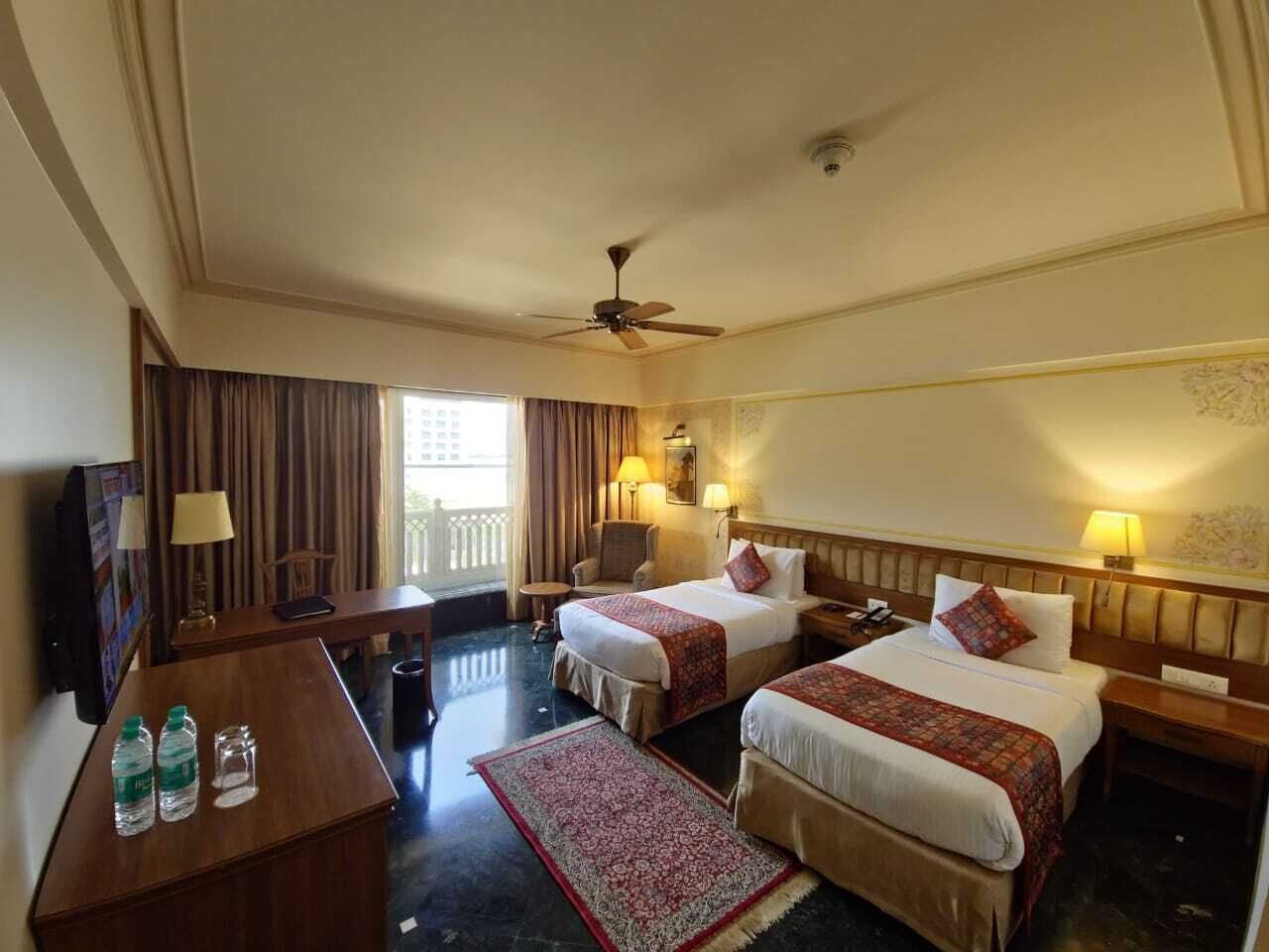 Habitación de hotel con dos camas, un escritorio, una silla, un televisor y un ventilador de techo.