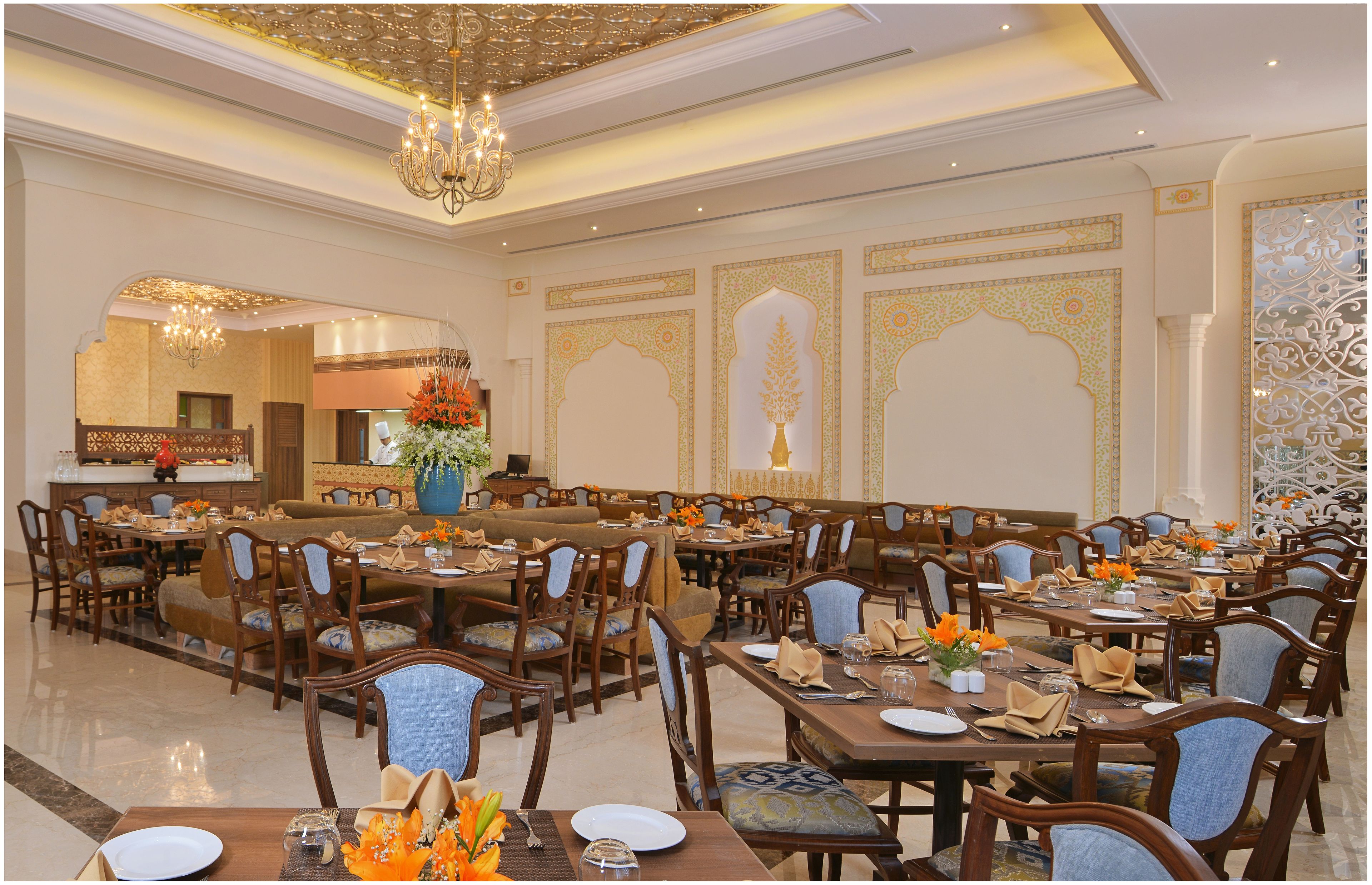 A spacious dining area with multiple tables and chairs, ornate wall decorations, and a chandelier.