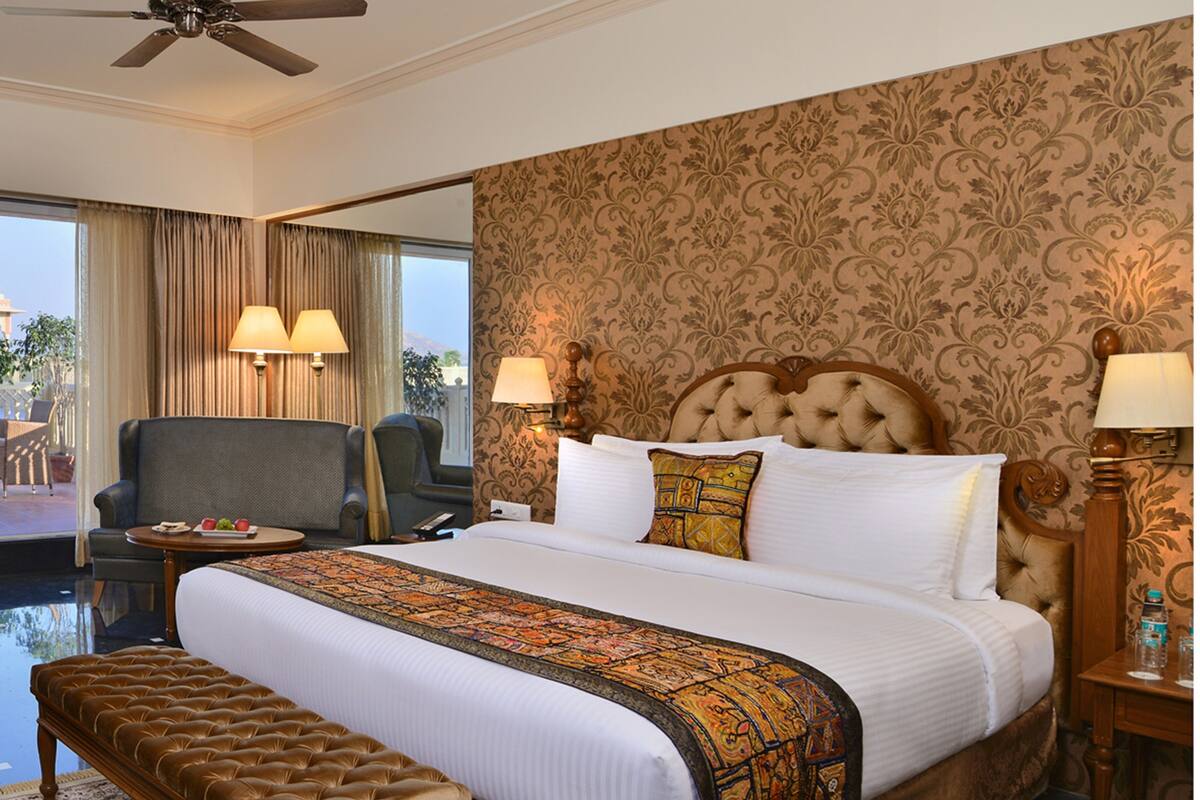A hotel room with a large bed, a sitting area with a chair and a table, and a view of the outdoors.