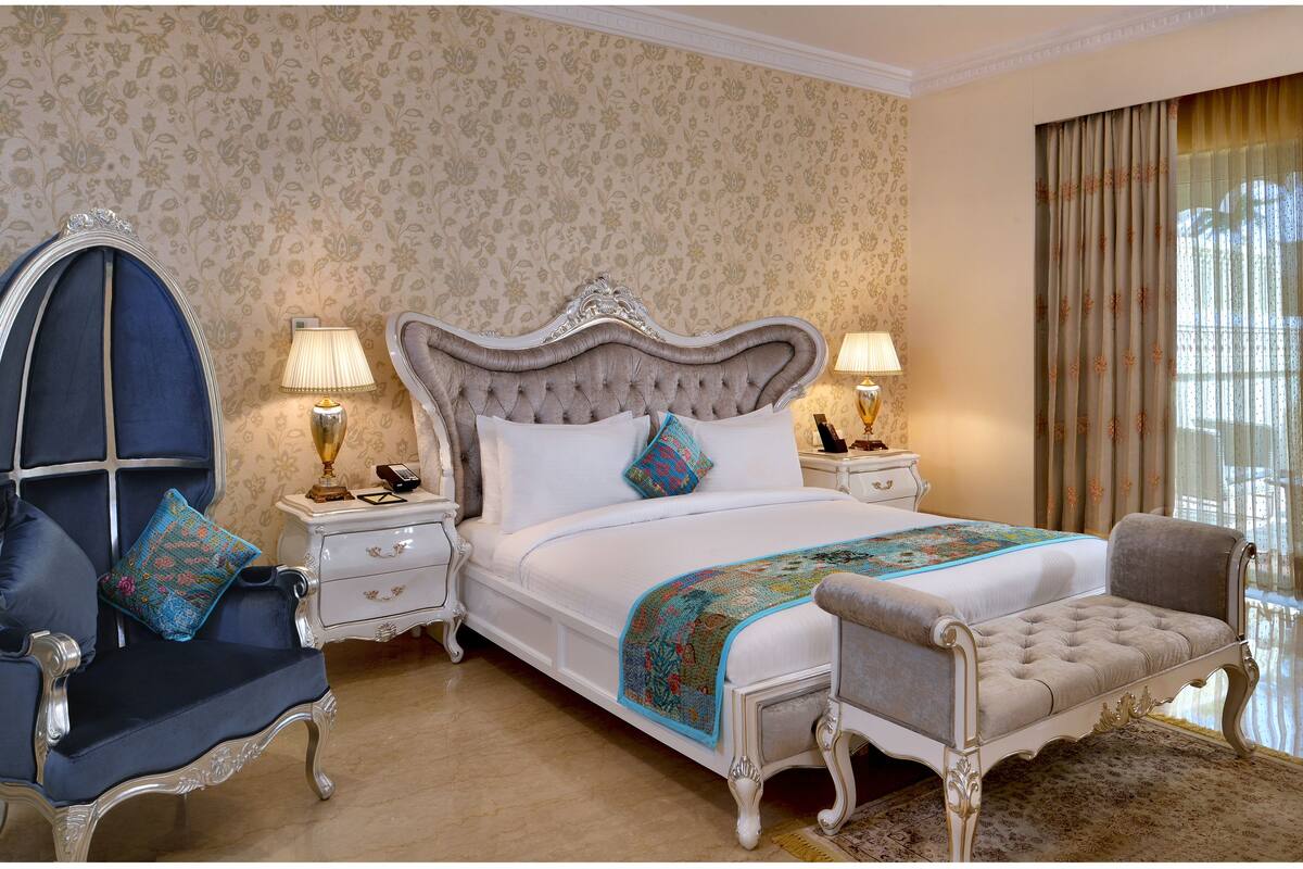 A luxurious bedroom with a large bed, ornate nightstands, a classic armchair, and a bench.