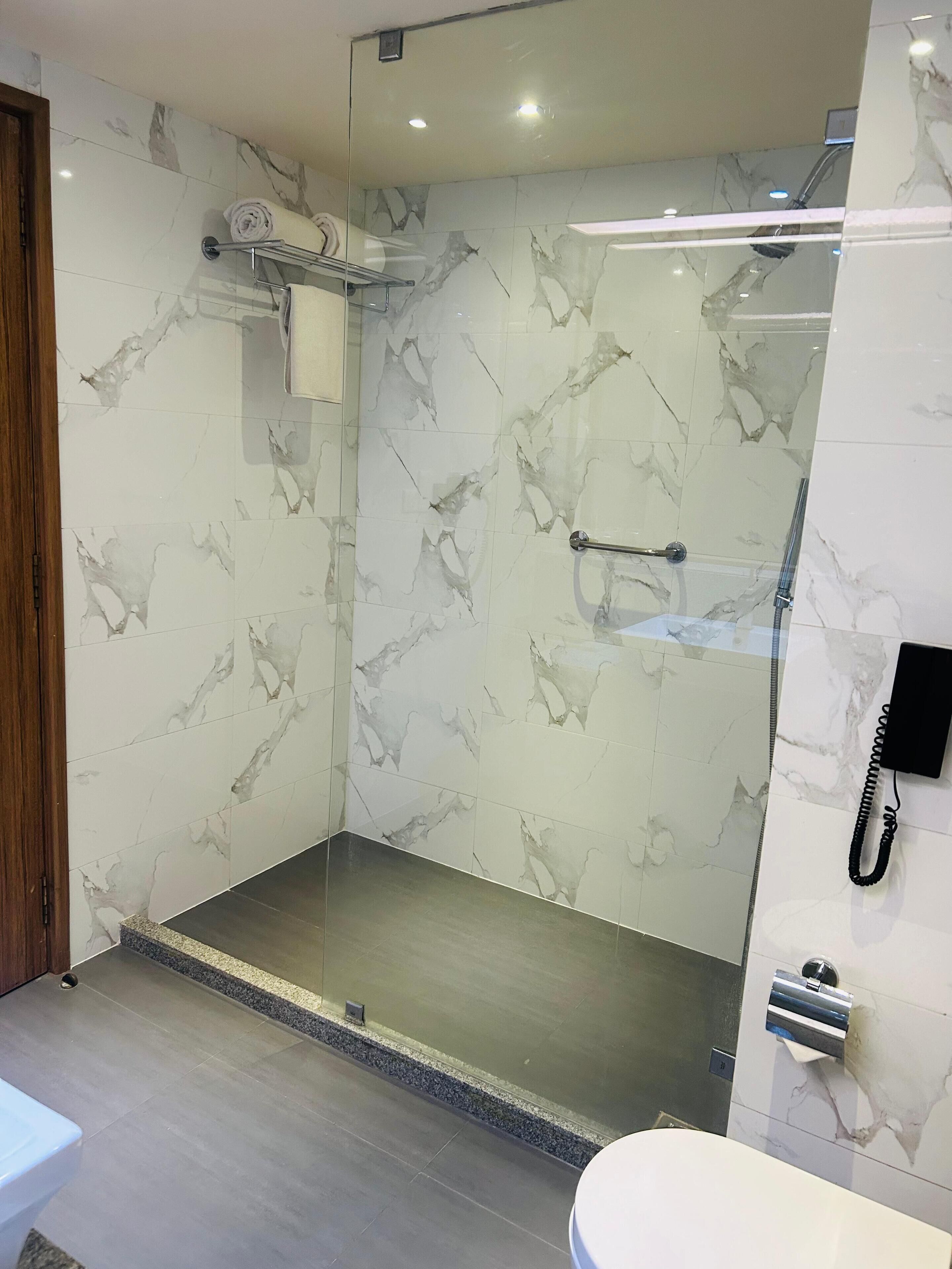 Un baño moderno con paredes de mármol, ducha con mampara de vidrio, inodoro y barra para toallas.