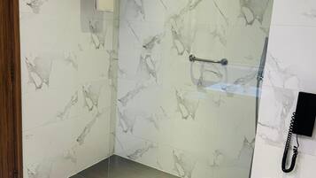 Un baño moderno con paredes de mármol, ducha con mampara de vidrio, inodoro y barra para toallas.
