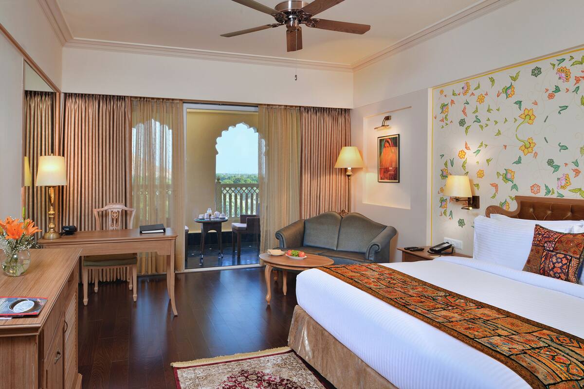 A hotel room with a bed, a desk, a chair, a small table, and a balcony.