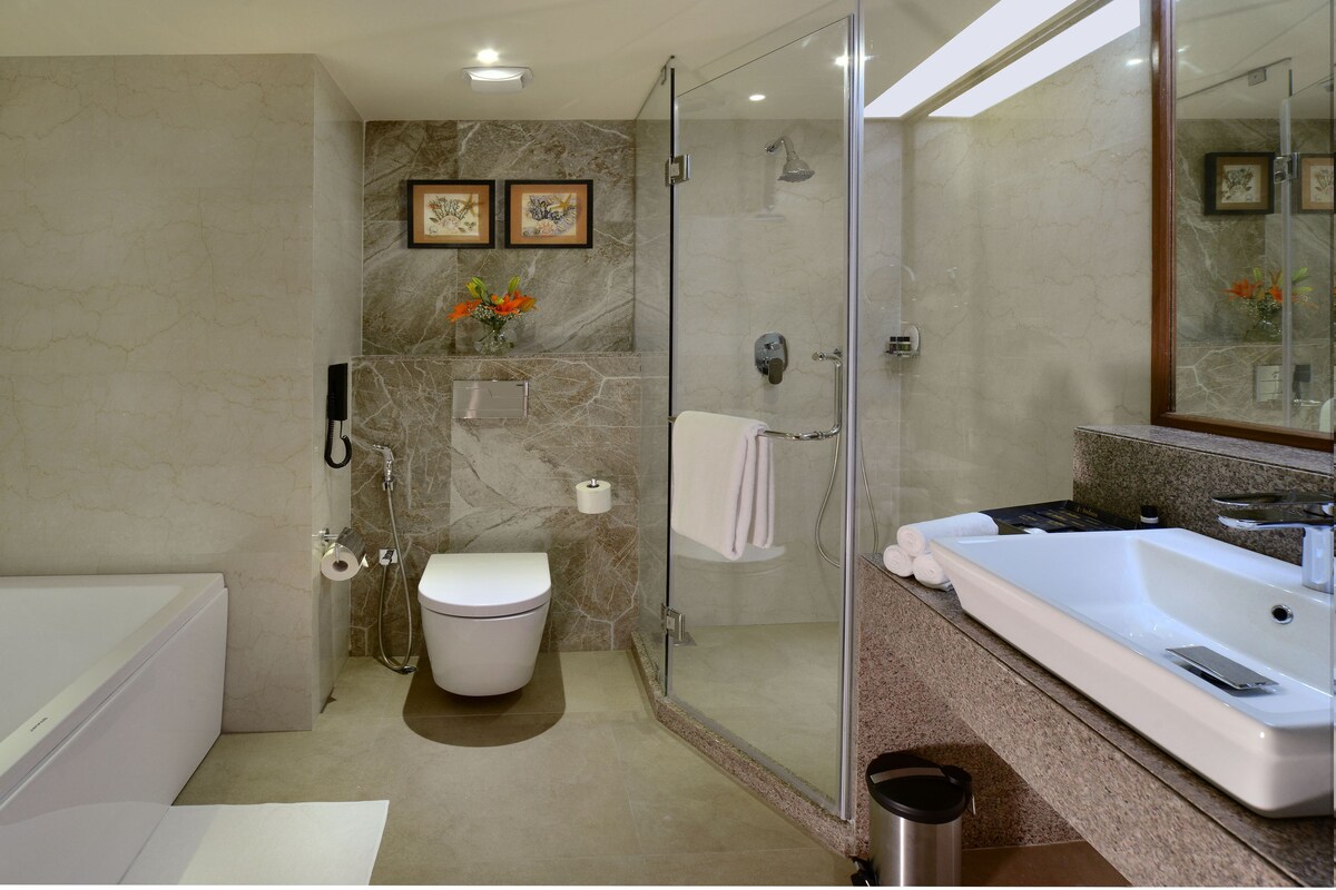 A modern bathroom with a glass-enclosed shower, a toilet, a bathtub, and a large mirror.