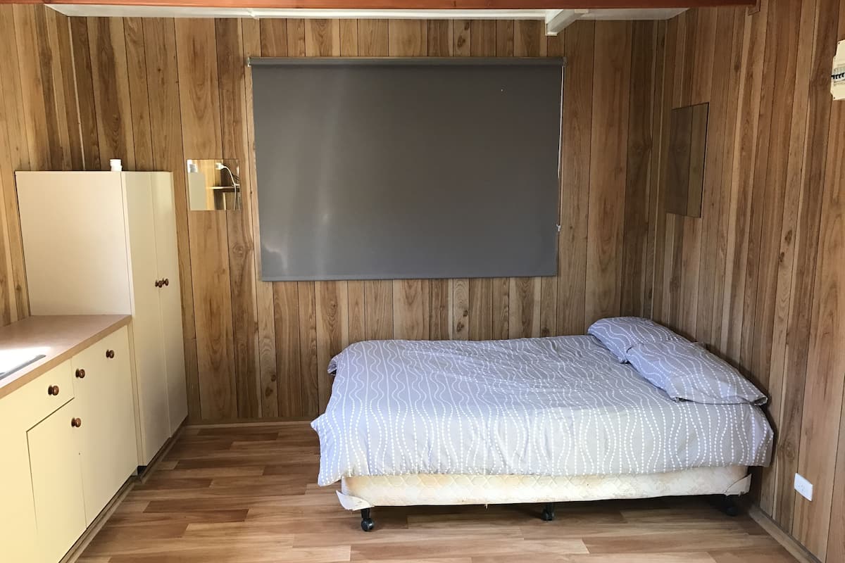A bedroom with a bed, wooden walls, a white wardrobe, and a large window.