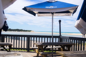 Un pontile in legno con un ombrellone blu e bianco, tavoli di legno e vista sulla spiaggia.