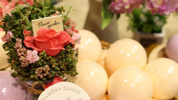 Une présentation de bombes de bain aux couleurs pastel, agrémentée d’une petite composition florale et d’une étiquette indiquant « Bombe de bain de qualité supérieure ».