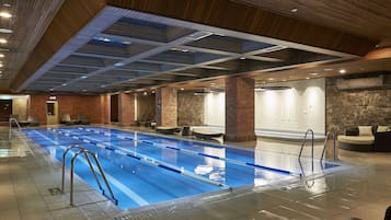Una amplia piscina interior con divisiones claras para carriles, una pared de ladrillo y una pared de piedra al fondo.