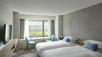 Habitación de hotel con dos camas, un escritorio, sillas, un televisor y una ventana con cortinas.