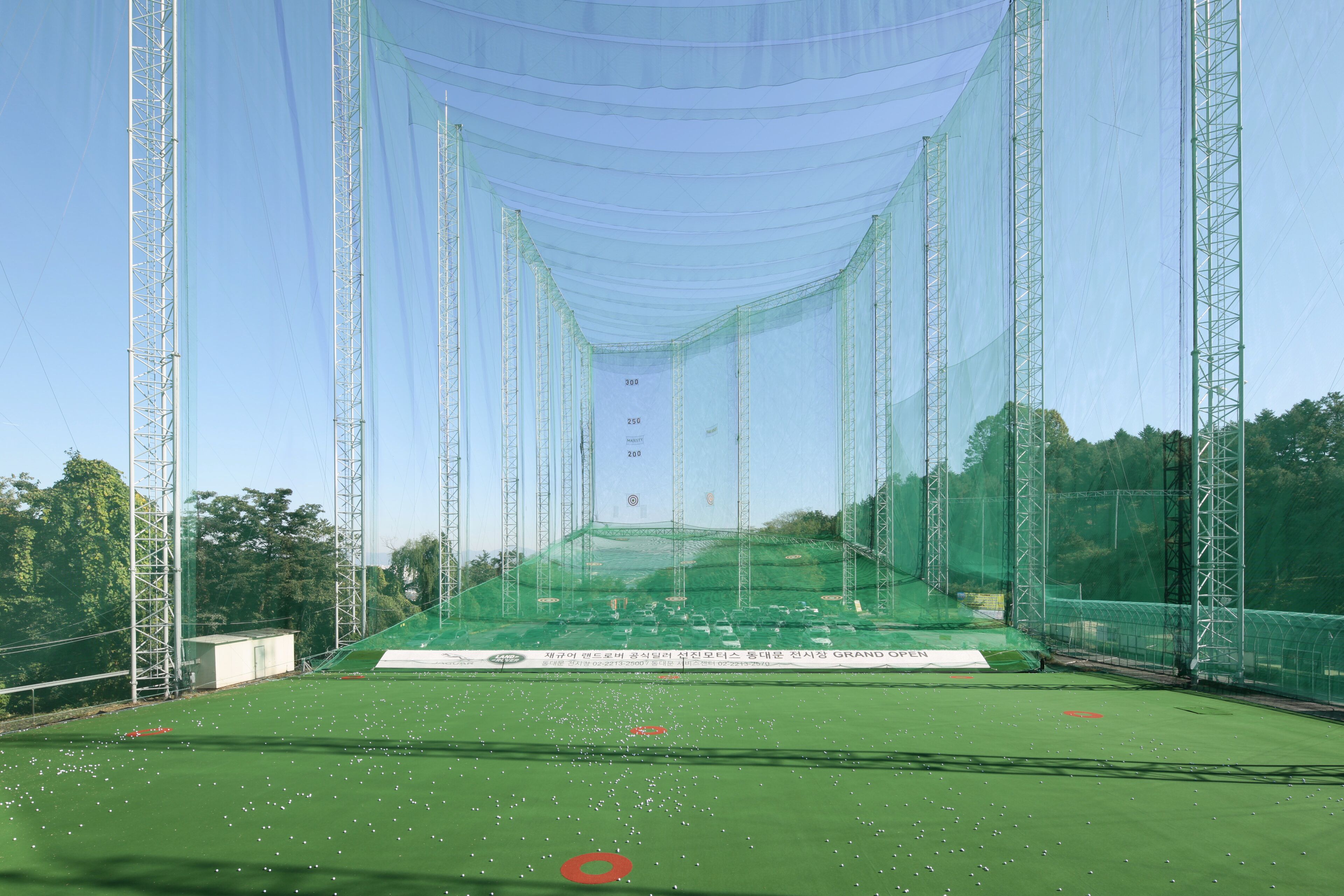 A cricket pitch with a netted enclosure, surrounded by tall metal structures.
