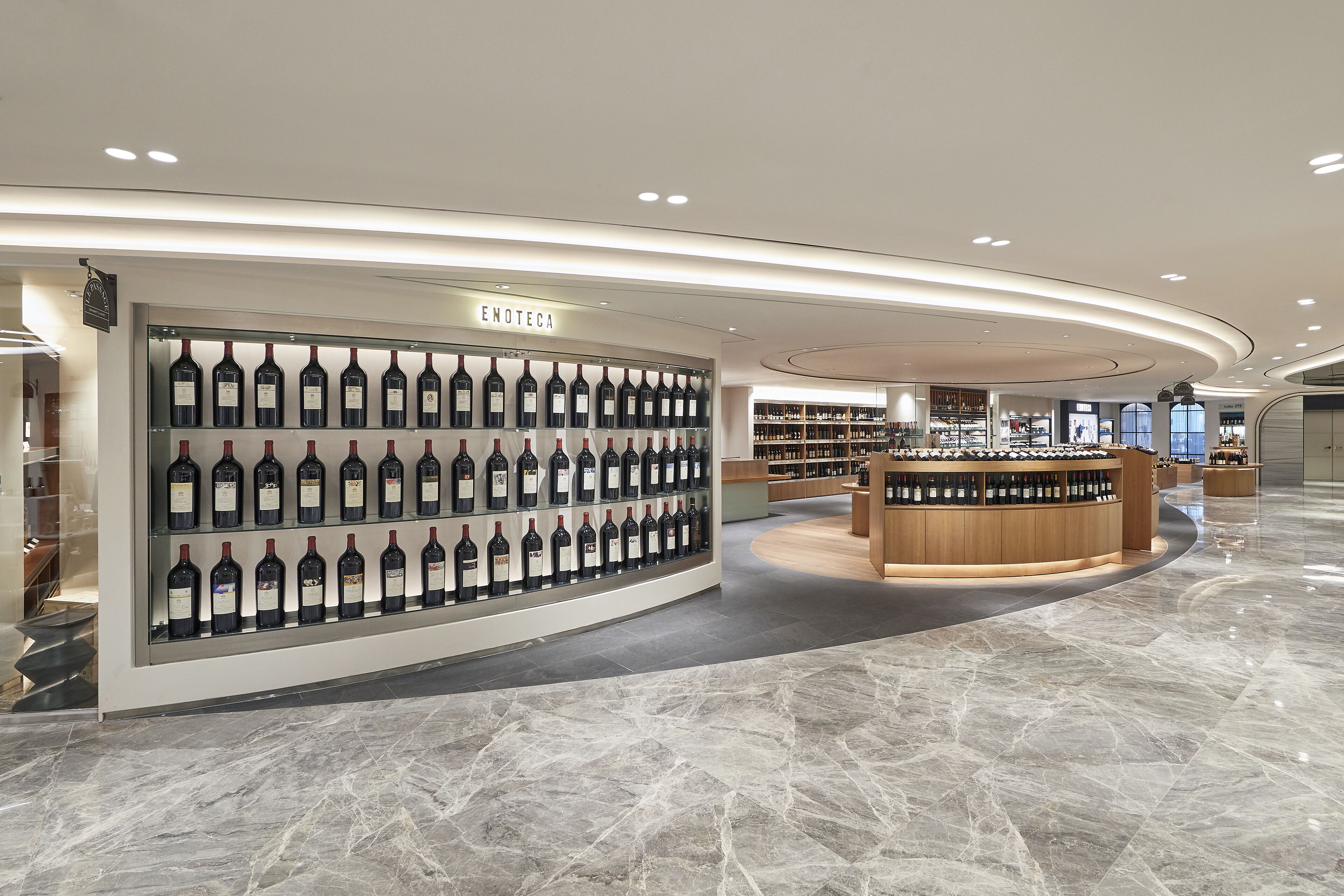 A modern wine store with a glass display of various wines and a wooden counter area.