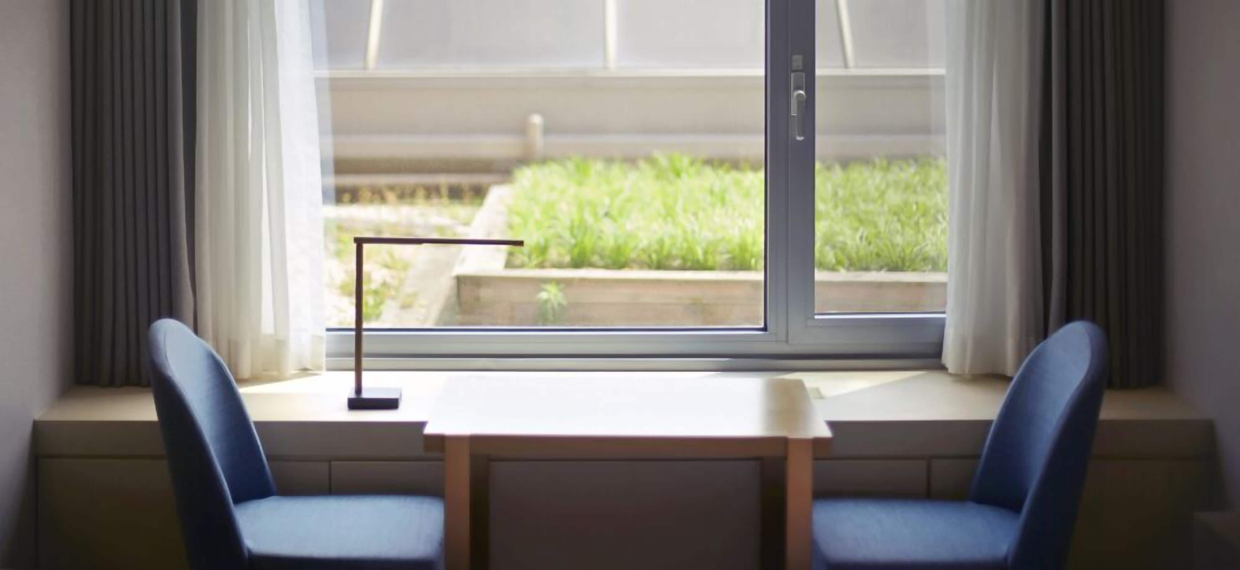 Ein Zimmer mit Fensterbank, zwei Stühlen, einem Tisch und einer Stehlampe.
