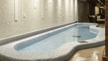 Una piscina interior moderna con suelo de baldosas y techo de madera.