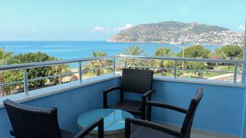 Un balcon agrémenté de fauteuils en osier et d’une table en verre, offrant une vue sur une ville côtière et la mer.
