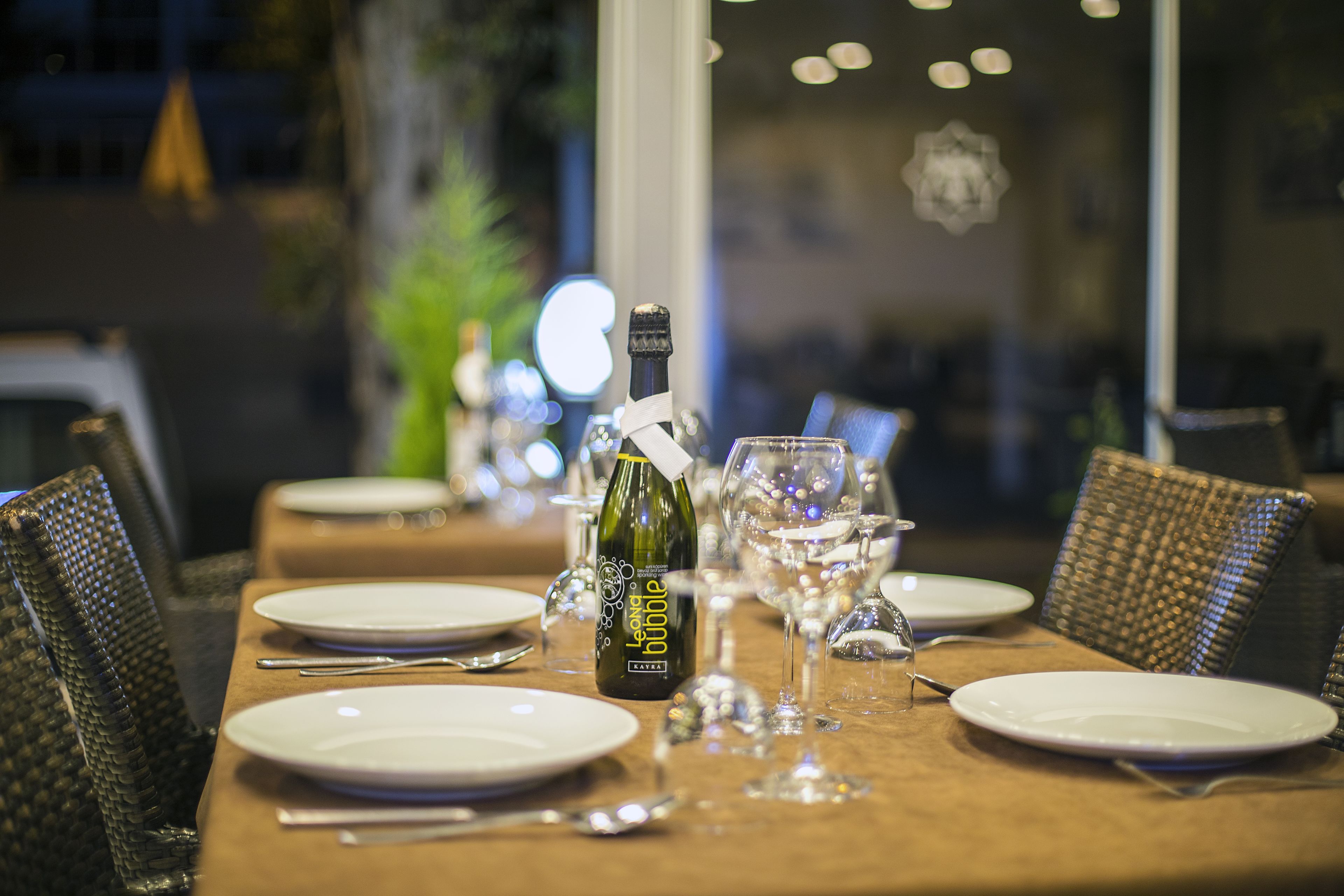 A dining table set with plates, cutlery, and a bottle of champagne.