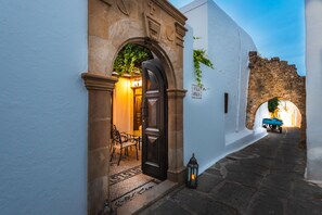 Un estrecho callejón empedrado con un arco rústico que conduce a un edificio con un cartel que dice 