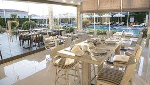 A spacious outdoor dining area with multiple tables and chairs, overlooking a swimming pool and lounge area. - Lagaria Apartments (Kassandra)