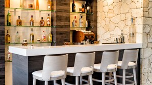 A bar area with a white countertop, multiple shelves with bottles, and three bar stools. - Lagaria Apartments (Kassandra)