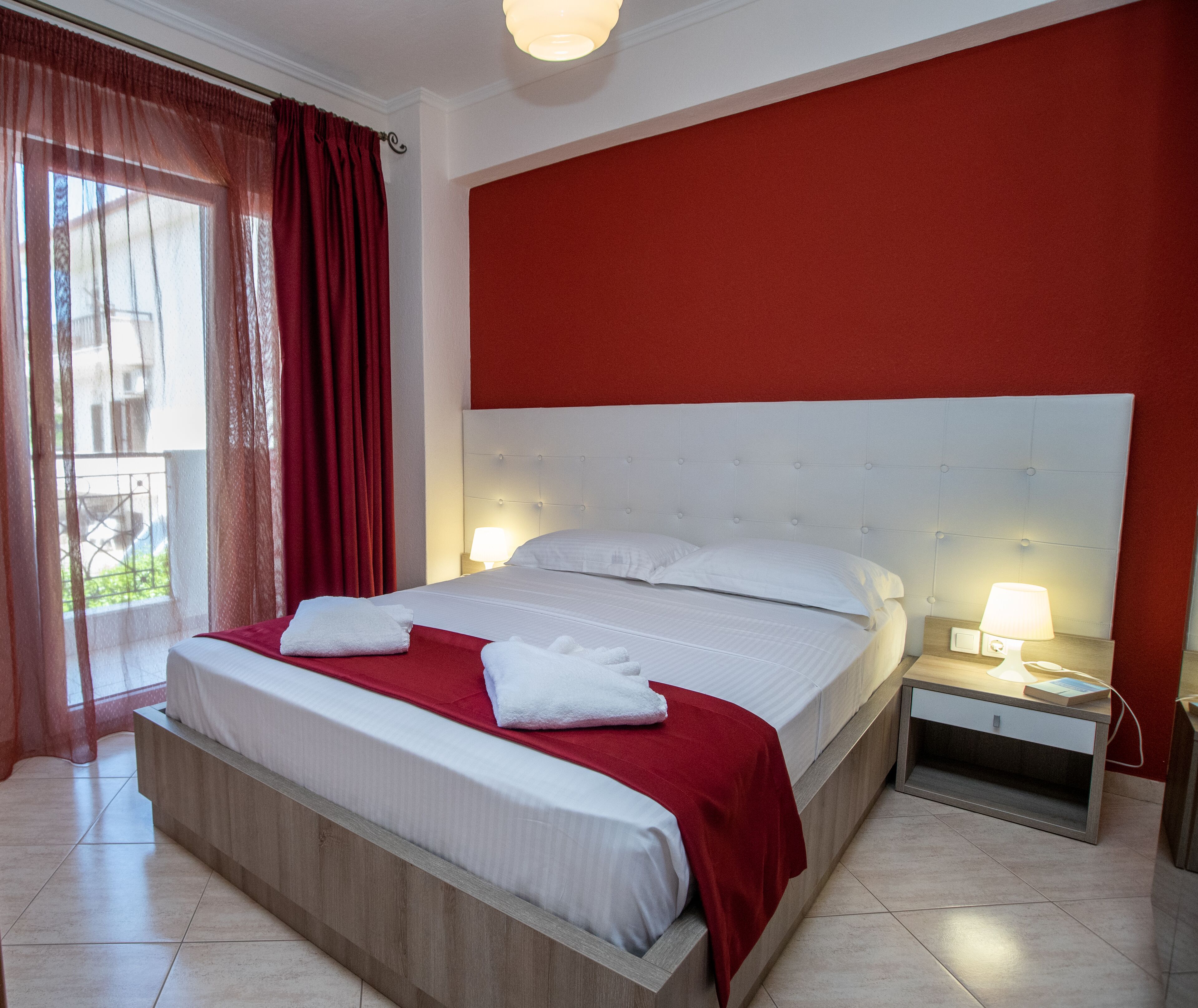 A hotel room with a large bed, red curtains, a red accent wall, and two bedside lamps.