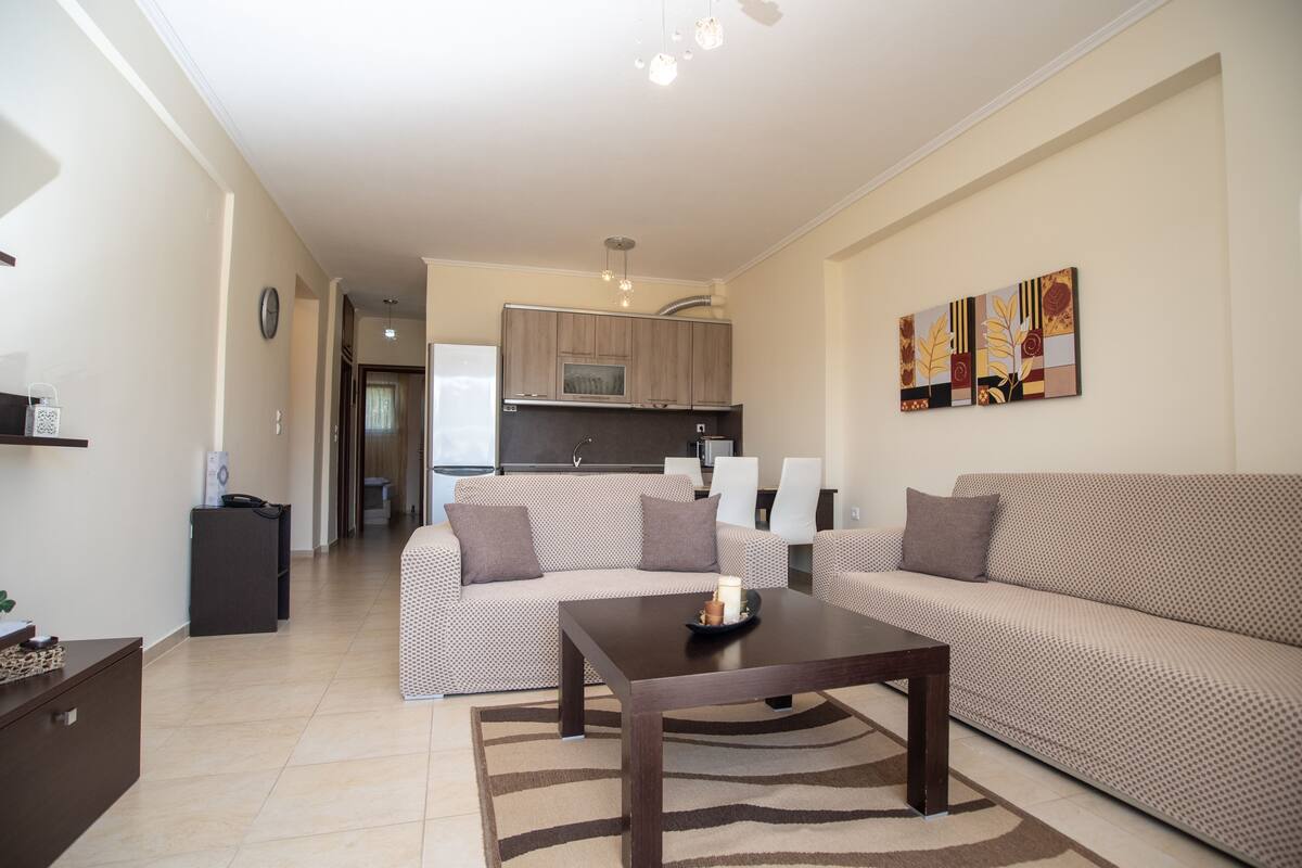 A modern living room with a sofa, a coffee table, and a kitchen in the background.