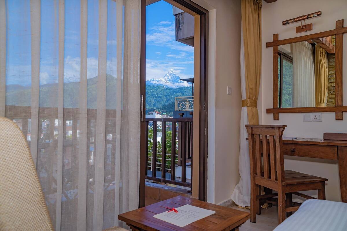 A hotel room with a balcony, a wooden desk, a chair, and a bed.