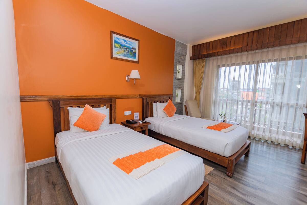 A hotel room with two beds, wooden headboards, a painting on the wall, a nightstand, and a window with curtains.