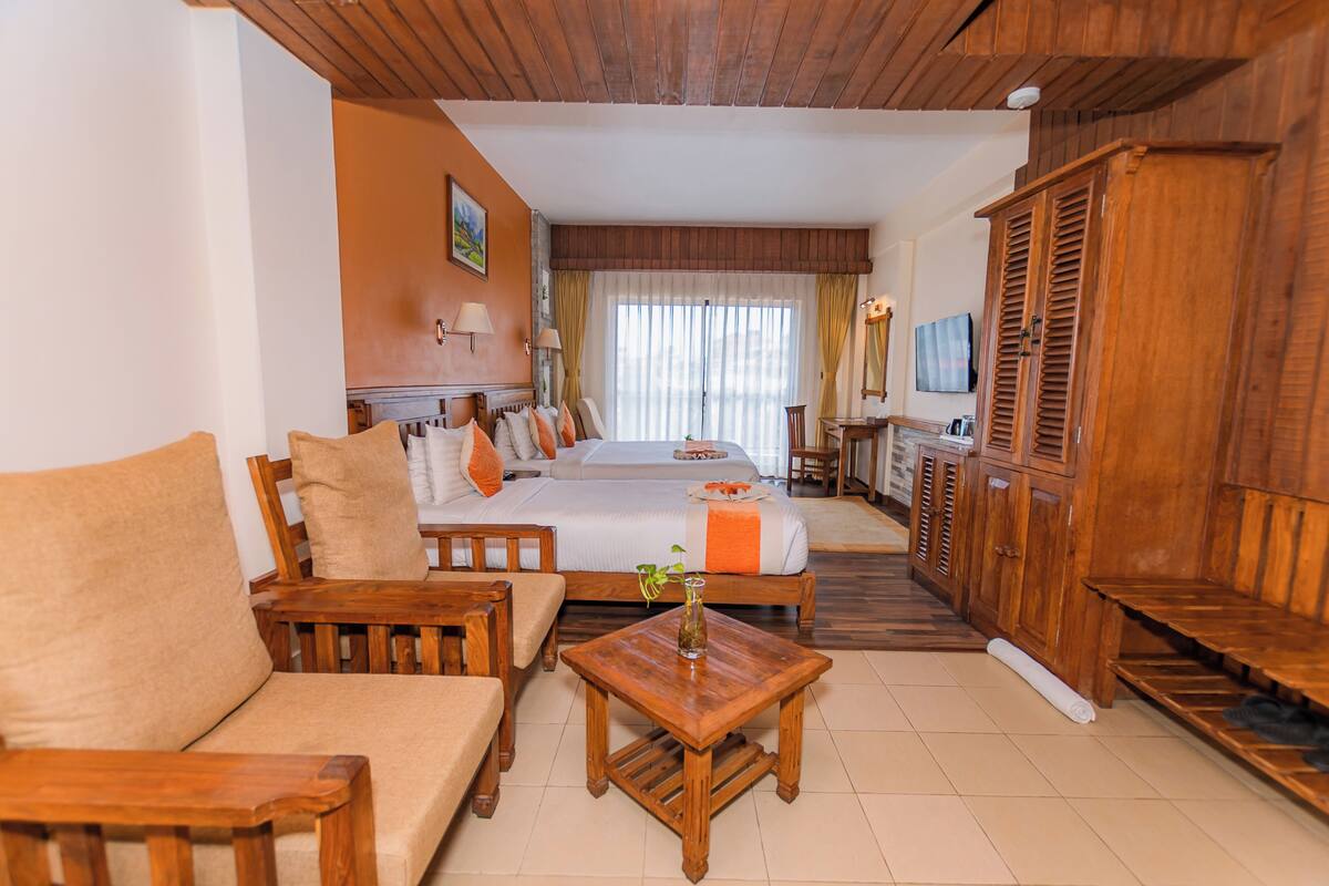 A hotel room with a bed, sofa, wooden furniture, a TV, and a mirror.