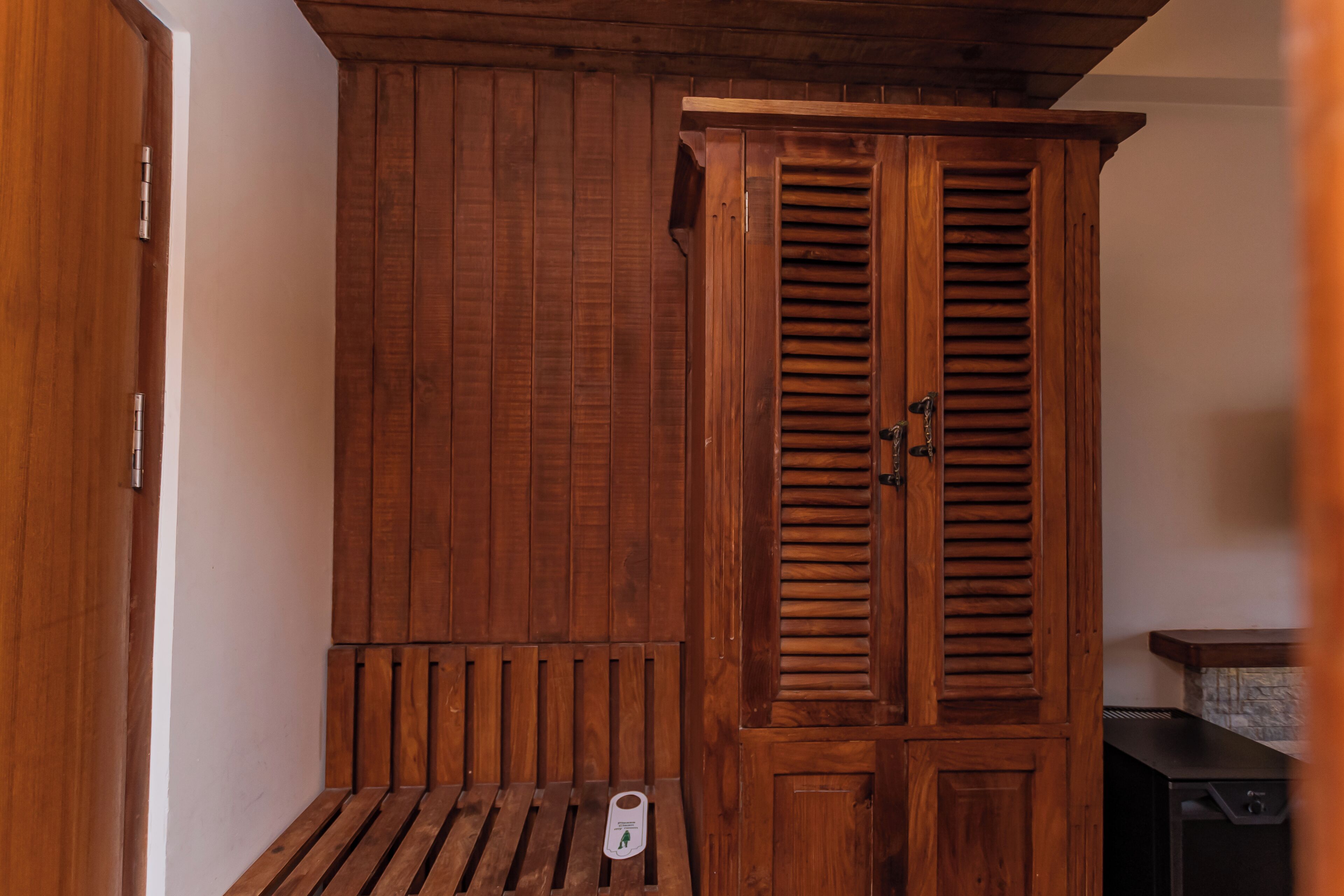 Un armario de madera con un banco, una mesita con una caja de pañuelos y un dispositivo electrónico negro.