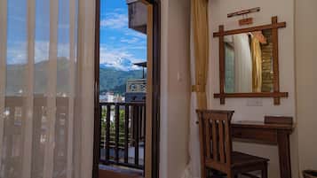 Une pièce avec un bureau en bois, une chaise, un miroir et une vue sur les montagnes, visible à travers une porte vitrée.